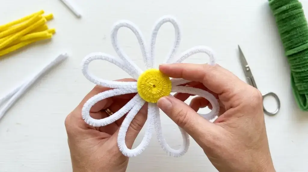 Assembling pipe cleaner daisy flower with white petals around yellow center