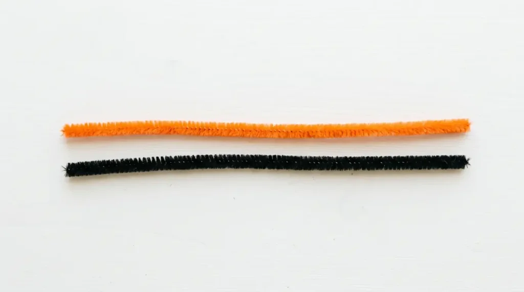 Two pipe cleaners needed to make a butterfly — one orange colored and one black, laid flat on a white surface