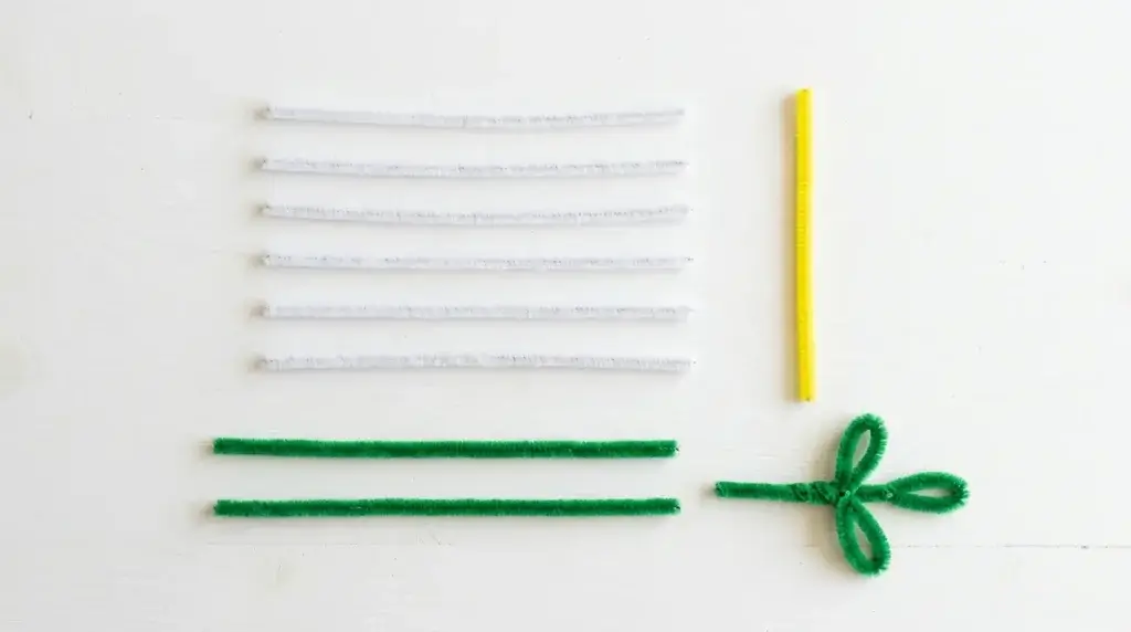 Materials needed to make a pipe cleaner lily — white and yellow pipe cleaners cut into pieces and two green pipe cleaners on a white surface