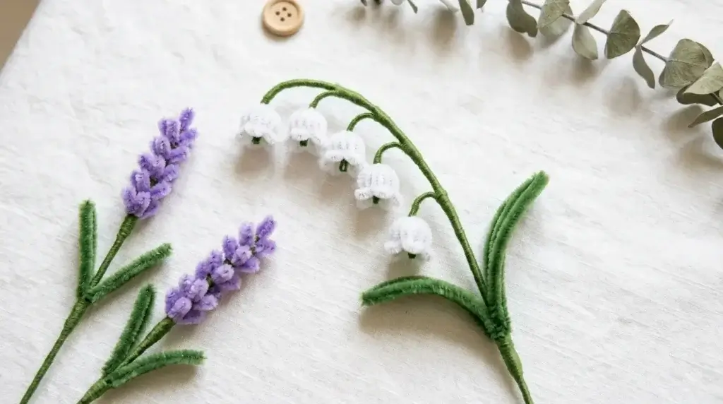 Miniature pipe cleaner lily of the valley with tiny white flowers cascading along a green stem, displayed next to lavender pipe cleaner sprigs