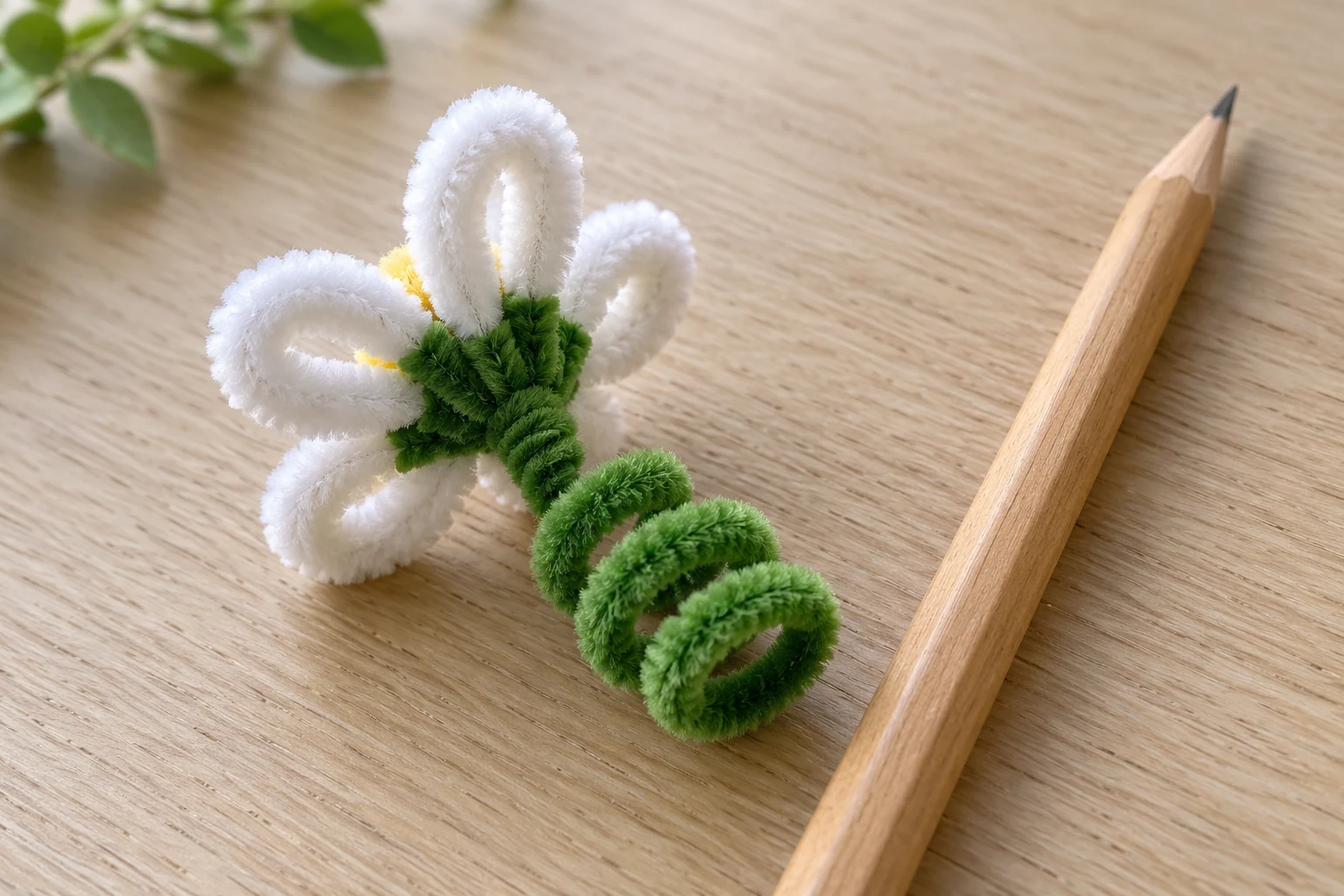Back of a white pipe cleaner flower with green wraps and an open coil beside a wooden pencil